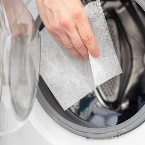 A hand dropping a dryer sheet into a washing machine