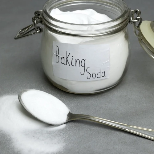A jar full of baking soda with a spoonful of baking soda next to it
