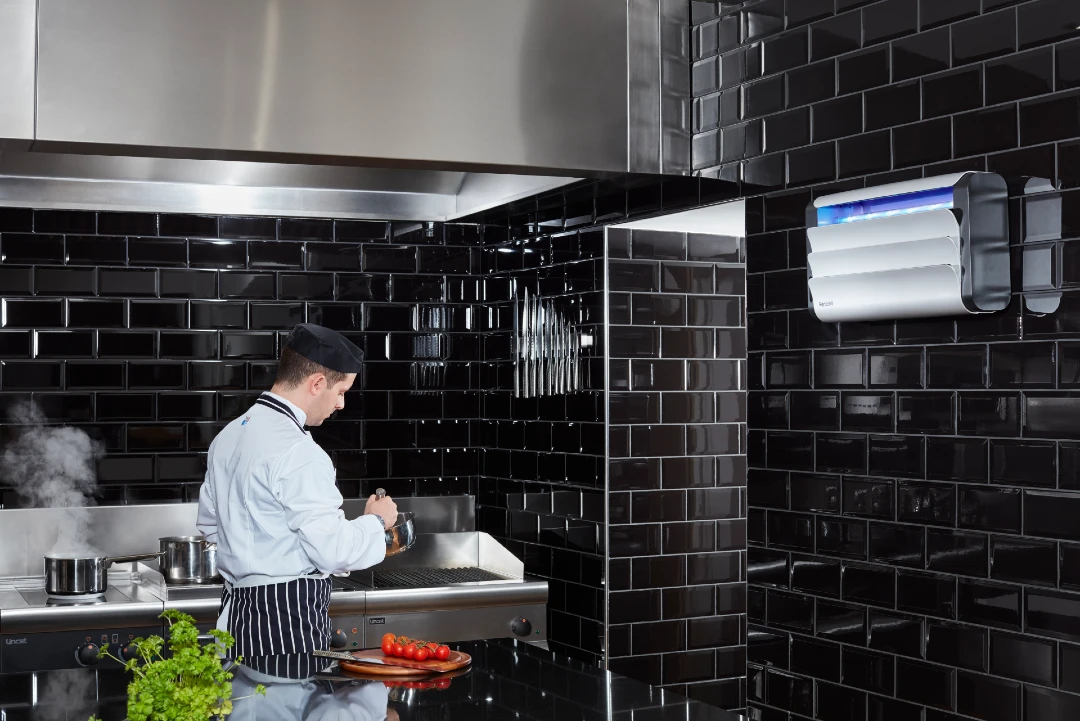 A Lumnia insect light trap on a black-tiled wall of a commercial kitchen, with a chef preparing food